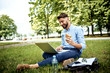 © baranq - Young businessman having sandwich for lunch in the park and working on laptop