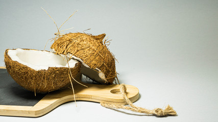 Coconut exotic fruit, two halves of fruit shell on a stone kitchen board with wooden handle blackboard, with a bright background, selective focus, selective light, close-up