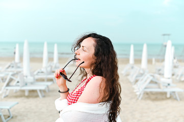 A woman in a red dress and curly hair is standing on the beach. A man with happy emotions. Walk along the sea promenade. Travel and tourism in the summer. Copy space