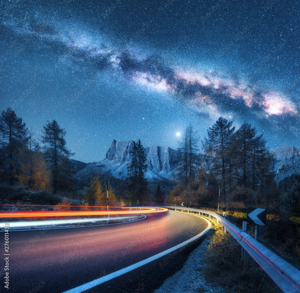 Milky Way over mountain road. Blurred car headlights on winding road in ...