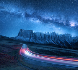 milky way over mountain road at night in summer. blurred car headlights on winding road. colorful la