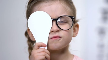 Wall Mural - Pretty female child in eyeglasses covering eye examination tool, medical test