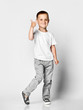 © FAB.1 - Little cute boy preschooler in a white T-shirt and gray pants on a light background, happily looking at the camera, showing a thumb sign cool