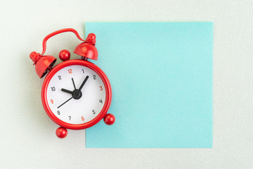 Flat lay of red alarm clock with blank sticky note for message on white background with copy space using as time, deadline, stop procrastination or schedule presentation wallpaper