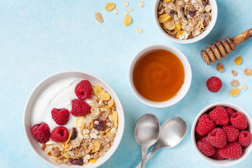 Wall Mural - Greek yogurt in bowl with ingredients raspberries, honey and muesli on blue table top view.