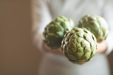 The girl holds in her hands an artichoke with a blur of the background, the concept of proper and dietary nutrition, dottex. horizontal picture