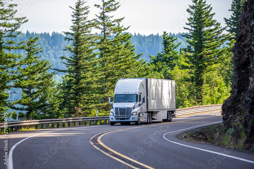 Fotografía White big rig semi truck transporting goods in refrigerated semi trailer turning