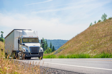 white big rig semi truck with day cab transporting cargo in bulk semi trailer driving uphill in Columbia Gorge