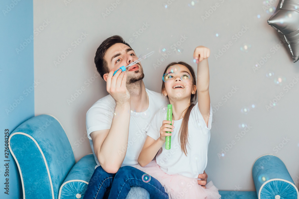 Happy father with daughter blowing bubbles at home, candid emotions.