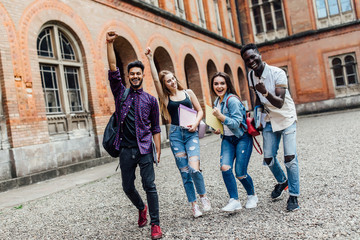 Wall Mural - Four students friends with smile happy emotions with raised hands up victory sign of pass exam outdoors at University.