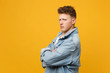 © ViDi Studio - Side view of sad offended young man in denim casual clothes looking camera, holding hands crossed isolated on yellow orange background. People sincere emotions lifestyle concept. Mock up copy space.