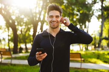 Poster - Portrait of caucasian athletic man listening to music with earphones and smartphone while doing workout in sunny green park