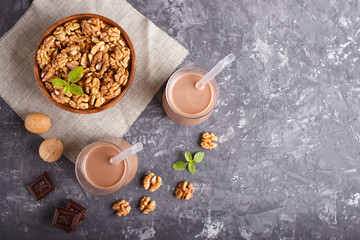 Organic non dairy walnut chocolate milk in glass and wooden plate with walnuts on a black concrete background.