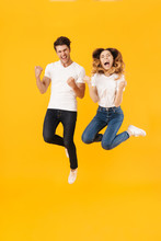 Full Length Portrait Of Joyful Couple Man And Woman In Basic T-shirts Rejoicing While Clenching Fists