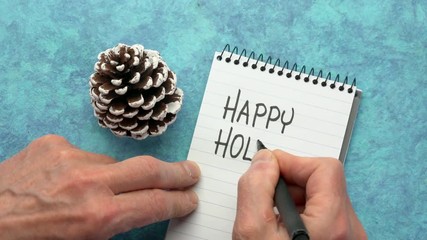 Canvas Print - happy holidays - man hand writing a note with a black marker in a spiral notebook, overhead view