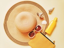 Summer Holidays Photo. Sun Hat, Yellow Clutch Bag, Sunscreen Lotion And Seashells. Flat Lay Fashion Photo. Beach Essentials