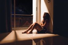 Sad And Depressed Young Woman Sitting On The Floor In The Living Room Looking Outside The Doors,sad Mood,feel Tired, Lonely And Unhappy Concept. Selective Focus