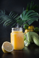 Wall Mural - Fresh summer fruits juice with banana, lemon on dark tropical background. Close up.