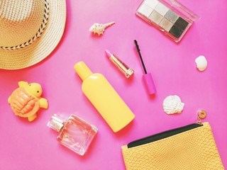 Wall Mural - Flat lay beauty photo. Sun hat, yellow sunscreen bottle, lipstick, mascara, eyeshadow, perfume and cosmetic bag on a pink background