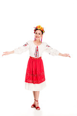 Wall Mural - full length view of happy brunette young woman in national Ukrainian costume doing welcome gesture isolated on white