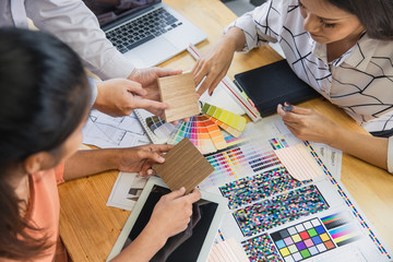 Architect designer Interior creative working hand drawing sketch plan and selection material color.  Young designers are using a laptop, discussing ideas and smiling while working in office.