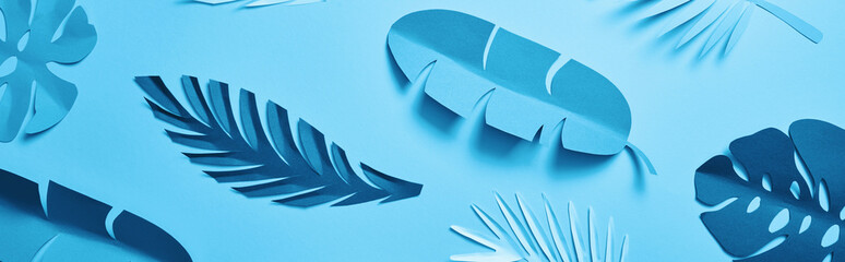 top view of blue exotic paper cut palm leaves on blue background with copy space, panoramic shot