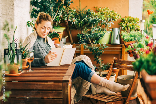 Cuadros en Lienzo Young beautiful woman relaxing on cozy balcony, reading a book, wearing warm kni