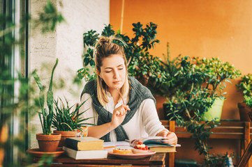 Young woman stuyding at home, sitting on the balcony, making notes in a nitebook