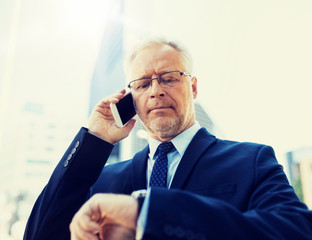 Poster - business, technology, time, punctuality and people concept - senior businessman calling on smartphone an looking at wristwatch or smart watch on his hand in city