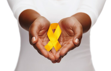 healthcare, charity and medicine concept - close up of woman cupped hands holding yellow gold childhood cancer awareness ribbon