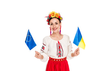 Wall Mural - happy brunette young woman in national Ukrainian costume holding European and Ukrainian flags isolated on white