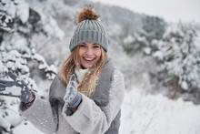 Conception Of Winter Holidays. Cheerful Girl In Warm Clothes Playing With Snow Outdoors Near The Beautiful Forest