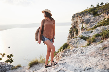 Wall Mural - Young girl with backpack enjoying sunset on peak of rocky mountain. Travel lifestyle adventure vacations concept