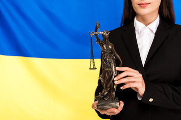 Wall Mural - cropped view of lawyer in black suit holding Themis statuette on Ukrainian flag background