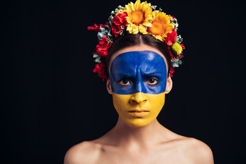 Wall Mural - sad naked young woman in floral wreath with painted Ukrainian flag on skin isolated on black