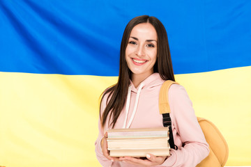 Wall Mural - smiling brunette young woman with backpack and books on Ukrainian flag background