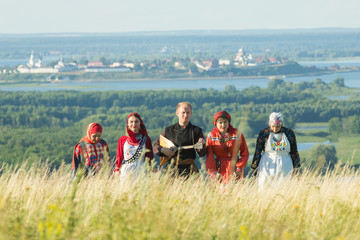 Wall Mural - People in traditional russian clothes walking on the field - a man holding a balalaika