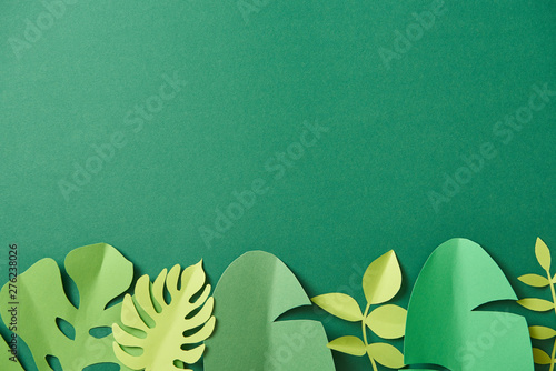 Fotomural top view of exotic paper cut palm leaves on green background with copy space
