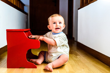 Wall Mural - Smiling baby playing a toy piano while learning music.