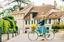 Retro Styled Portrait Of Beautiful Young Woman, Wearing Vintage Clothes, Holding Mint Color Bicycle With Yellow Flowers Placed In Basket