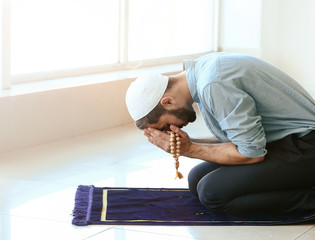 Young Muslim man praying indoors