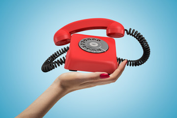 Wall Mural - side closeup of woman's hand facing up and holding ringing retro phone on light blue background.