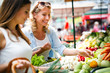 © NDABCREATIVITY - Young happy women shopping vegetables and fruits on the market