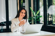 © bnenin - Elegant young woman using laptop and drinking coffee in modern office.