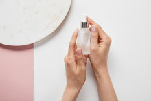 Cropped View Of Cropped View Of Woman Holding Cosmetic Glass Bottle Near Plate On White Pink Surface