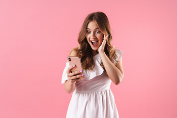 Wall Mural - Excited young pretty woman posing isolated over pink wall background using mobile phone chatting.