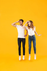 Full length portrait of young couple man and woman in basic t-shirts wondering while looking aside at copyspace