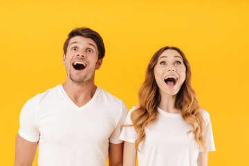 Sticker - Portrait of delighted couple man and woman in basic t-shirts wondering with open mouthes while looking upward at copyspace