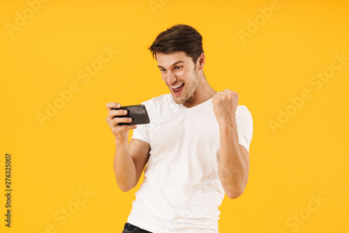 Photo of happy man in basic t-shirt rejoicing while playing video game on smartp Poster Mural XXL