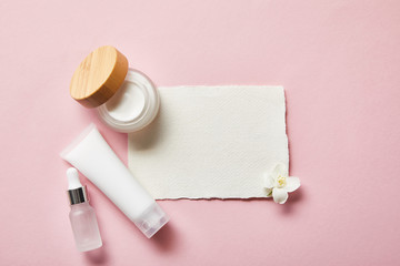 Canvas Print - top view of open jar with cream, cosmetic glass bottle, cream tube, piece of paper and jasmine flower on pink